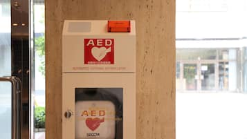 Kit di emergenza con defibrillatore automatico esterno montato su una parete, con segnale di avvertimento e maniglia.