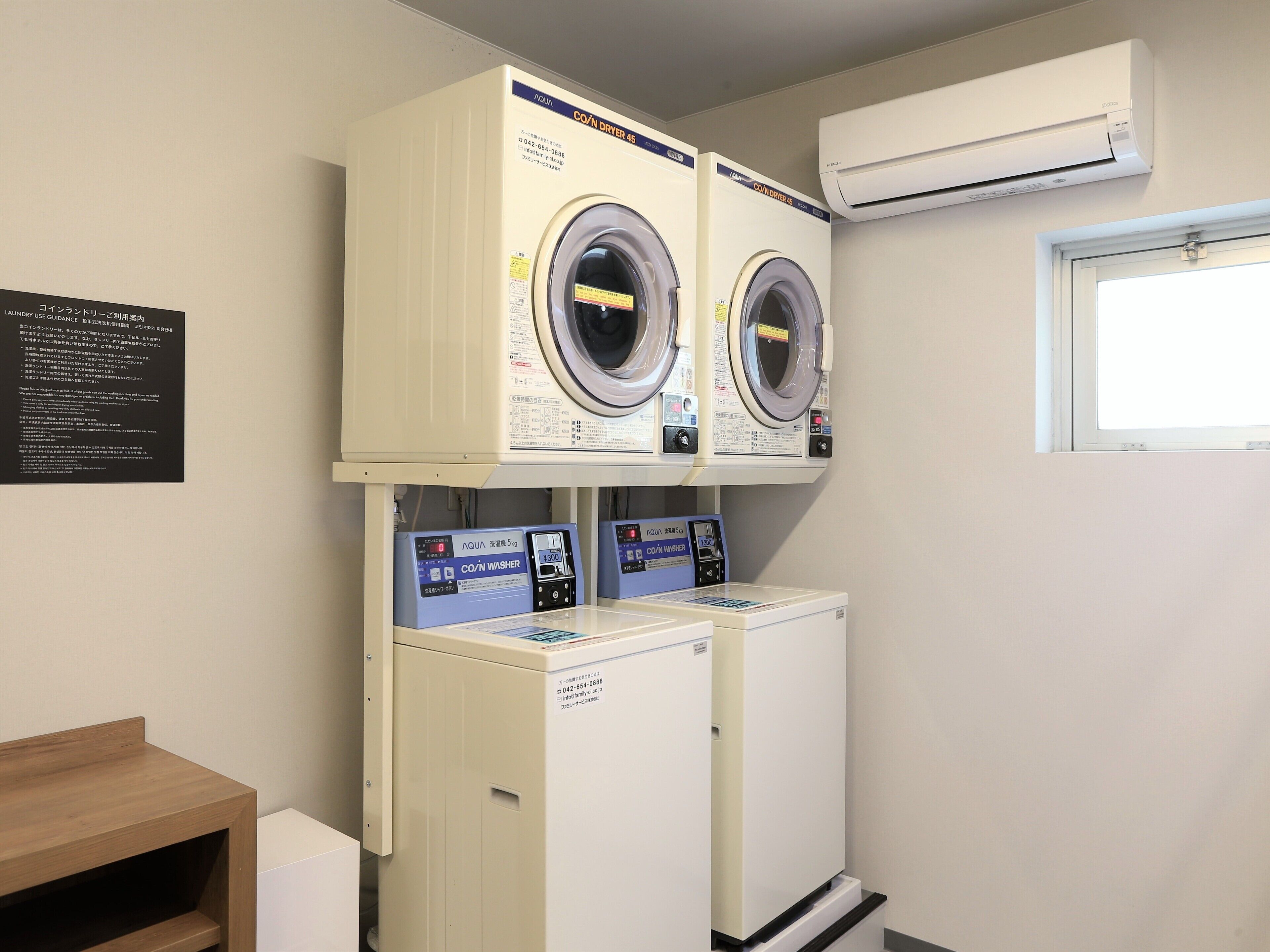 A laundry room with two front-loading washers and dryers, a wooden bench, and an air conditioning unit.