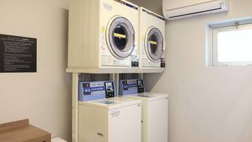 A laundry room with two front-loading washers and dryers, a wooden bench, and an air conditioning unit.