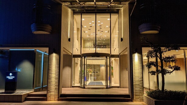 Une entrée d’hôtel moderne avec une porte en verre, un comptoir de réception bien visible et un escalier menant à l’entrée.