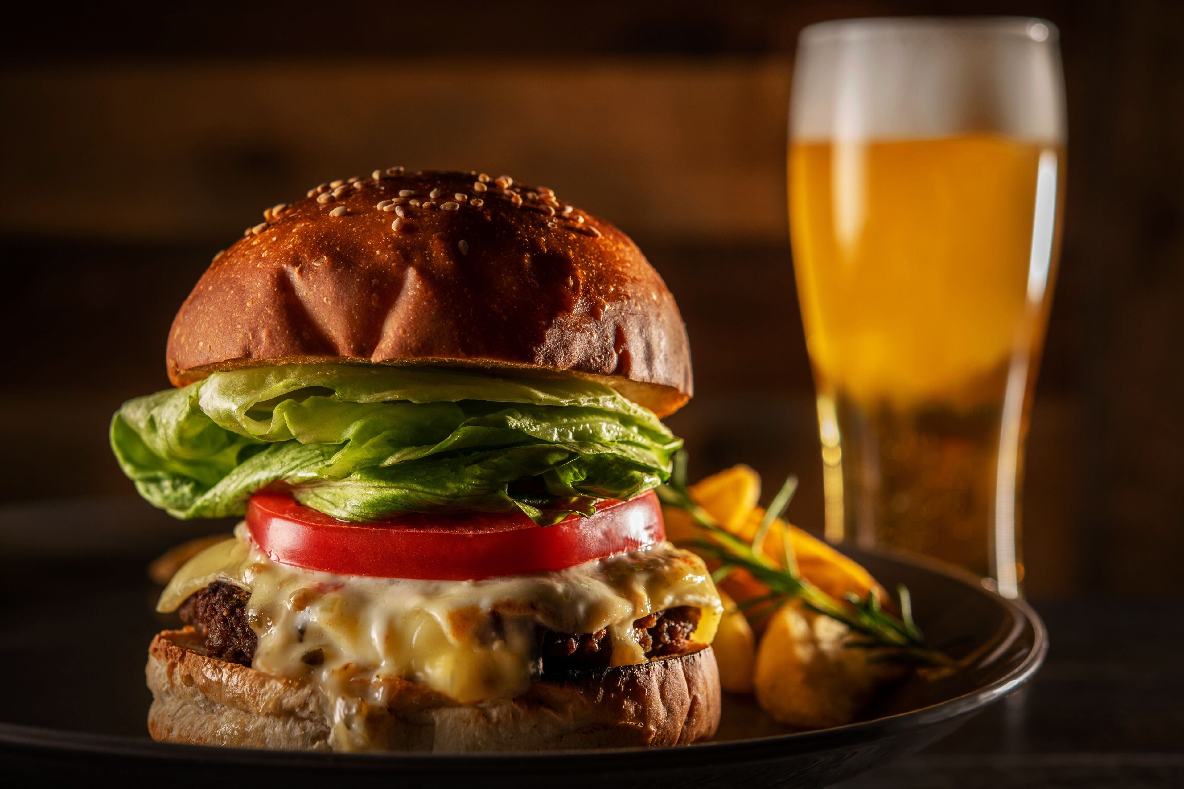 A burger with lettuce, tomato, and cheese, and a glass of beer on a plate.