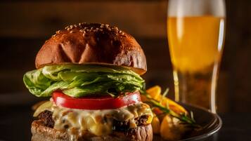 A burger with lettuce, tomato, and cheese, and a glass of beer on a plate.