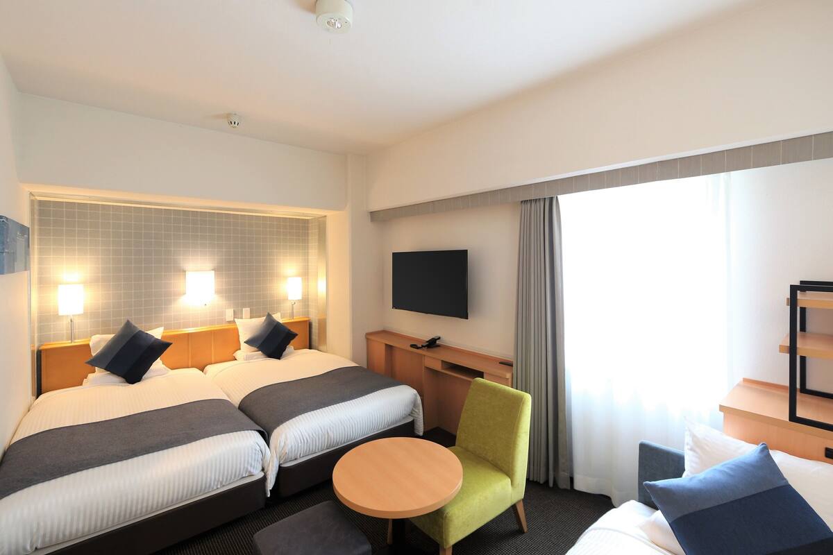 A hotel room with two beds, a TV, a desk, and a chair.