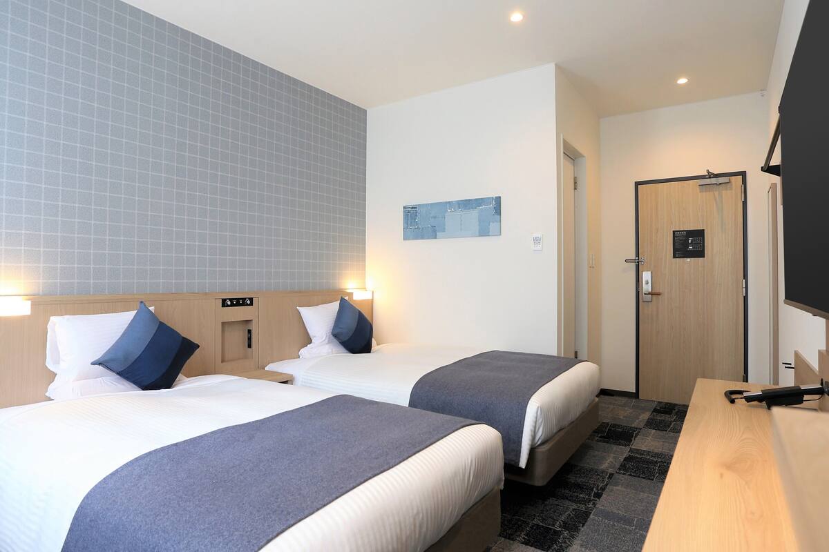 A hotel room with two beds, a wooden desk, a small table, and a door.