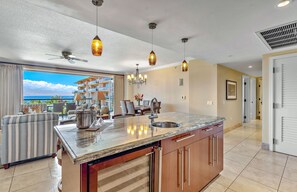 A modern kitchen with a large island, pendant lights, and a view of the ocean.