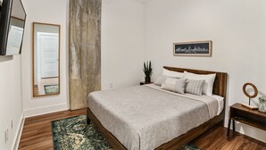 Une chambre à coucher avec un lit en bois, un tableau représentant un paysage urbain accroché au mur, un ventilateur de plafond et un grand miroir.