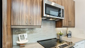 Une cuisine moderne avec des meubles en bois, un four à micro-ondes en acier inoxydable, une cuisinière encastrée et une petite plante en pot.