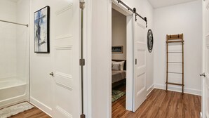 Un couloir avec des portes blanches, un plancher en bois, un lit avec une tête de lit et une échelle appuyée contre le mur.