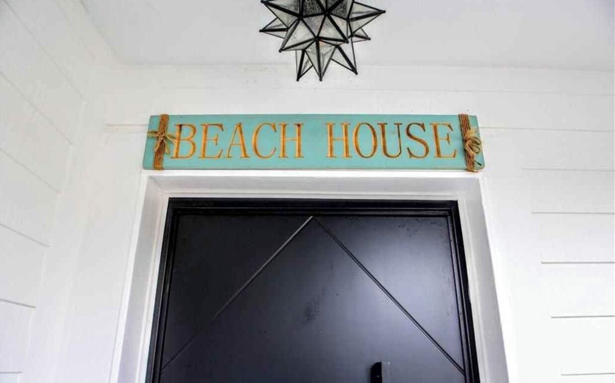 Une enseigne au-dessus d’une porte noire, sur laquelle on peut lire en lettres dorées sur un fond turquoise : « BEACH HOUSE ».