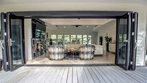 Une porte coulissante ouverte donne sur un coin repas avec une table et des chaises, et on aperçoit une cuisine au fond, ainsi qu’une vue sur l’extérieur.