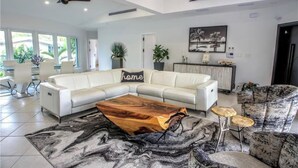 Un salon spacieux avec un canapé d’angle blanc, une table basse au design original en bois et un tapis à motifs.