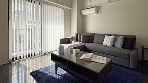 Una sala de estar moderna con un sofá gris, una mesa de centro y un ventanal con persianas.