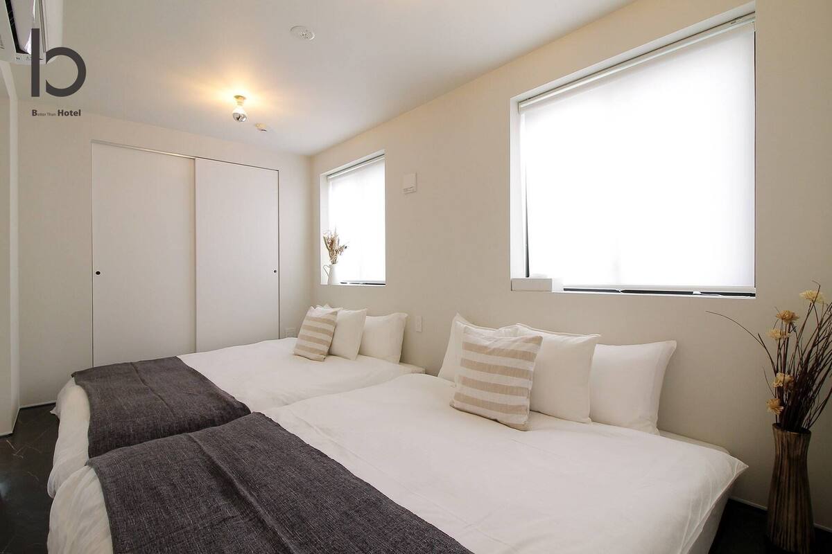 A hotel room with two beds, a large window, a vase with dried flowers, and a ceiling light.