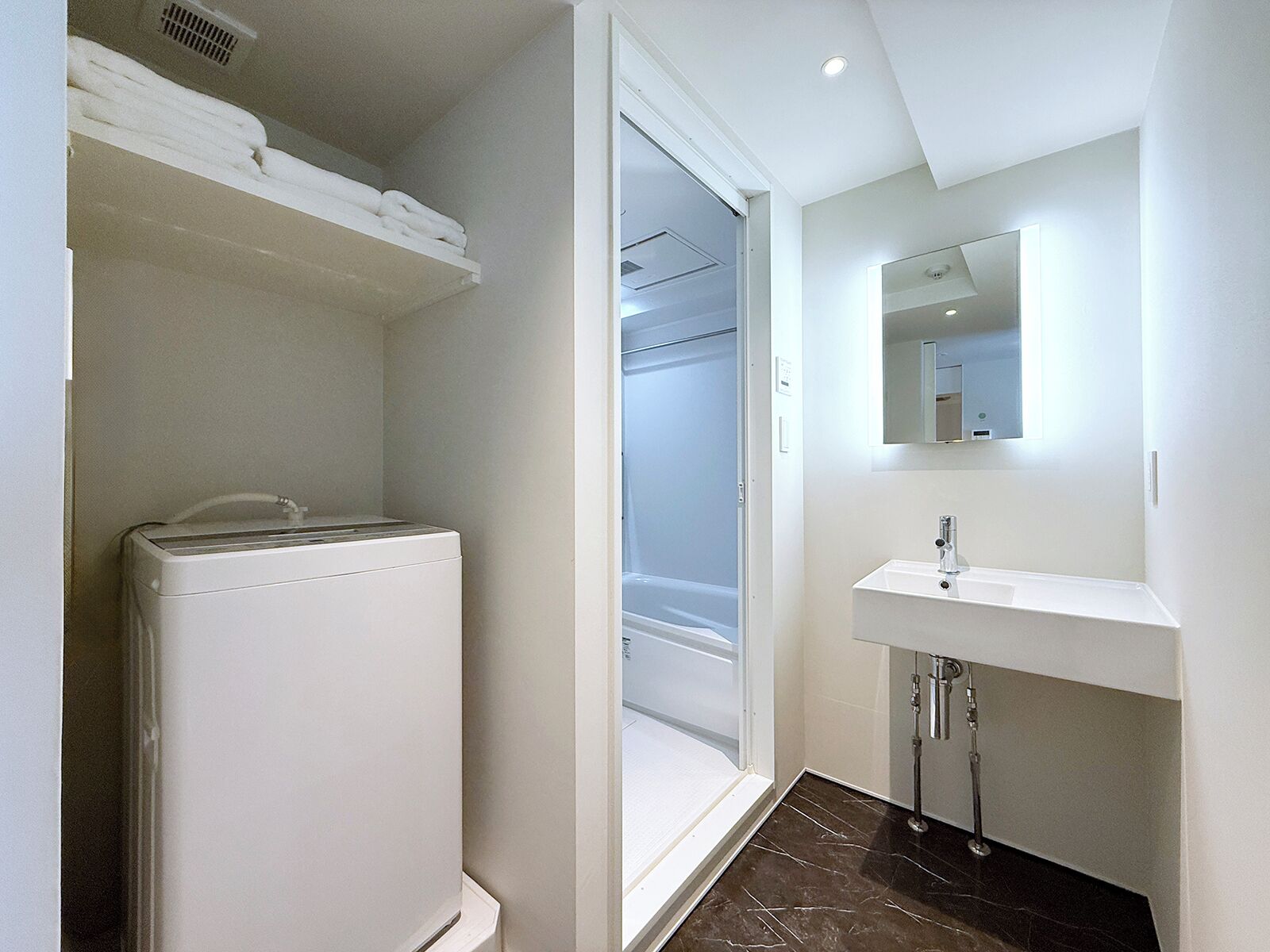 A modern bathroom with a built-in washer, a shower, and a sink with a mirror above it.