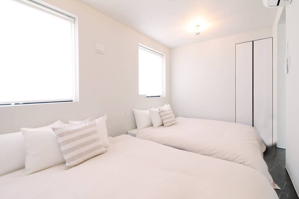 A bedroom with two beds, a wardrobe, and a window.