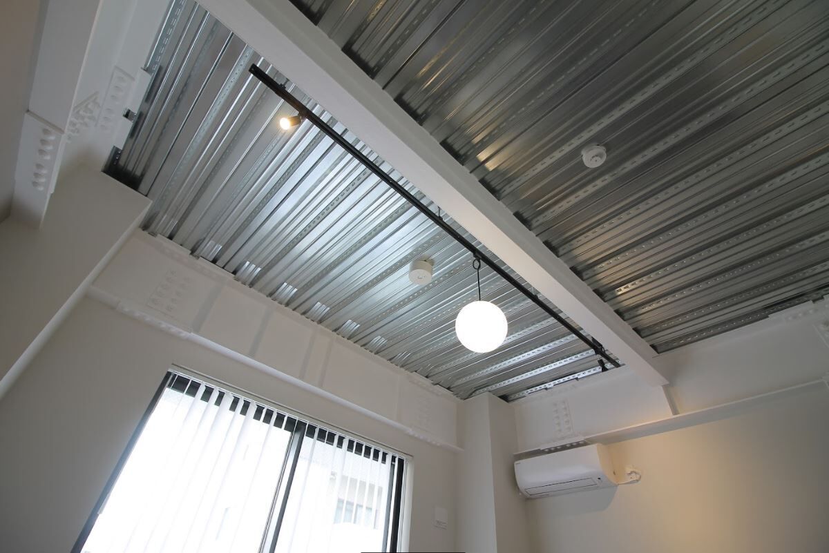 A room with a high ceiling, visible ductwork, a hanging light fixture, and a window with blinds.