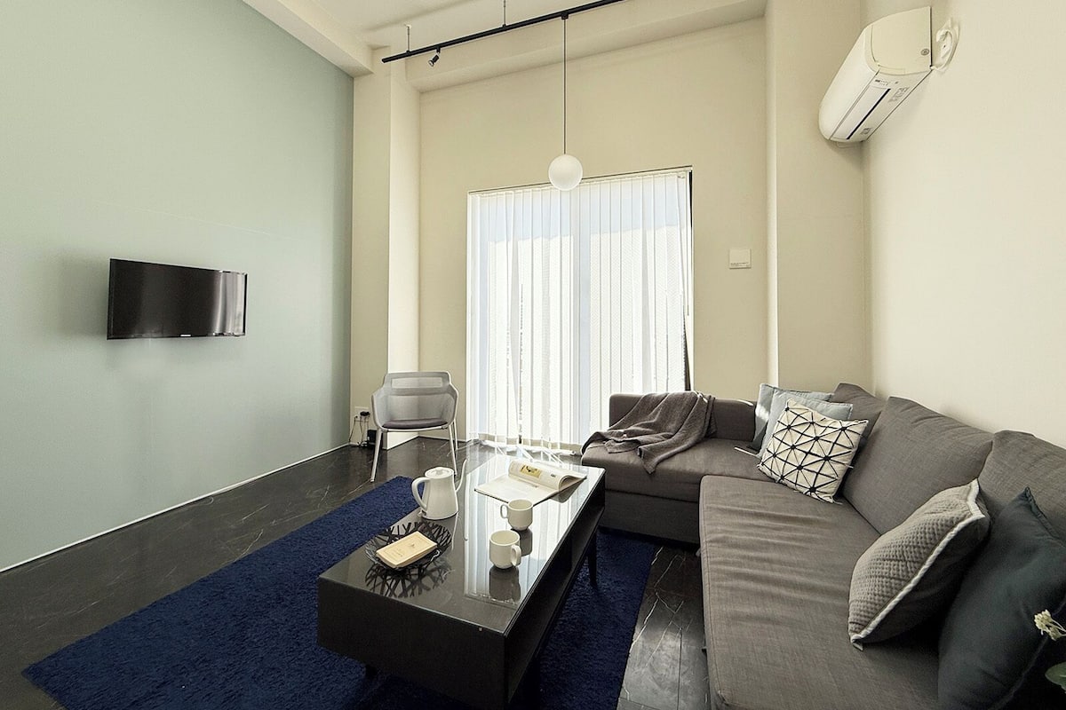 A modern living room with a sofa, a coffee table, a chair, and a TV mounted on the wall.