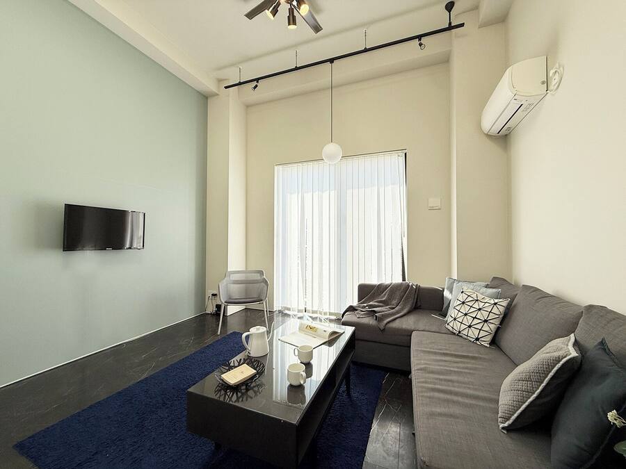 A modern living room with a sofa, a coffee table, a chair, and a TV mounted on the wall.