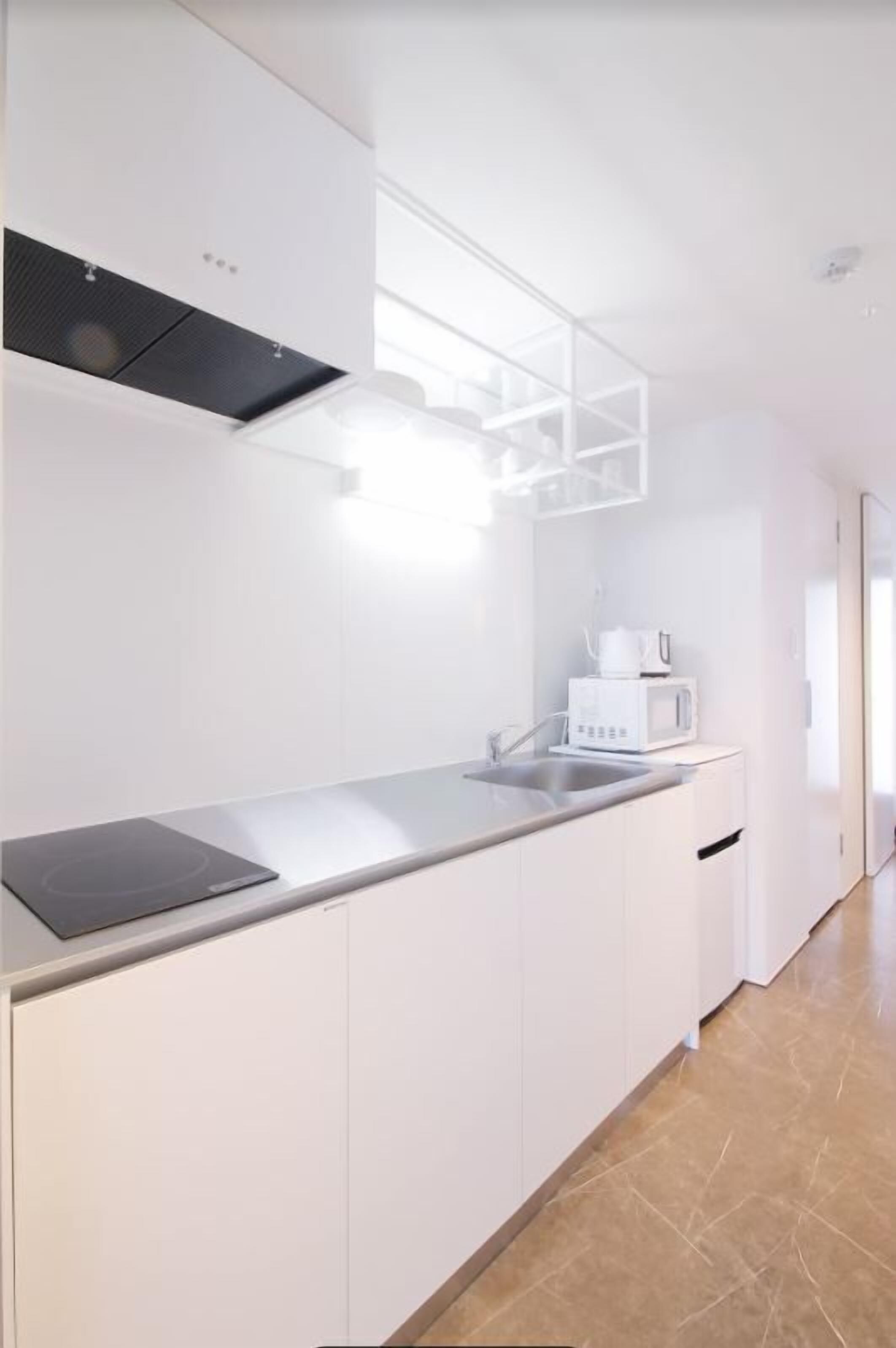 A modern kitchen with white cabinetry, a stainless steel countertop, and a built-in microwave.