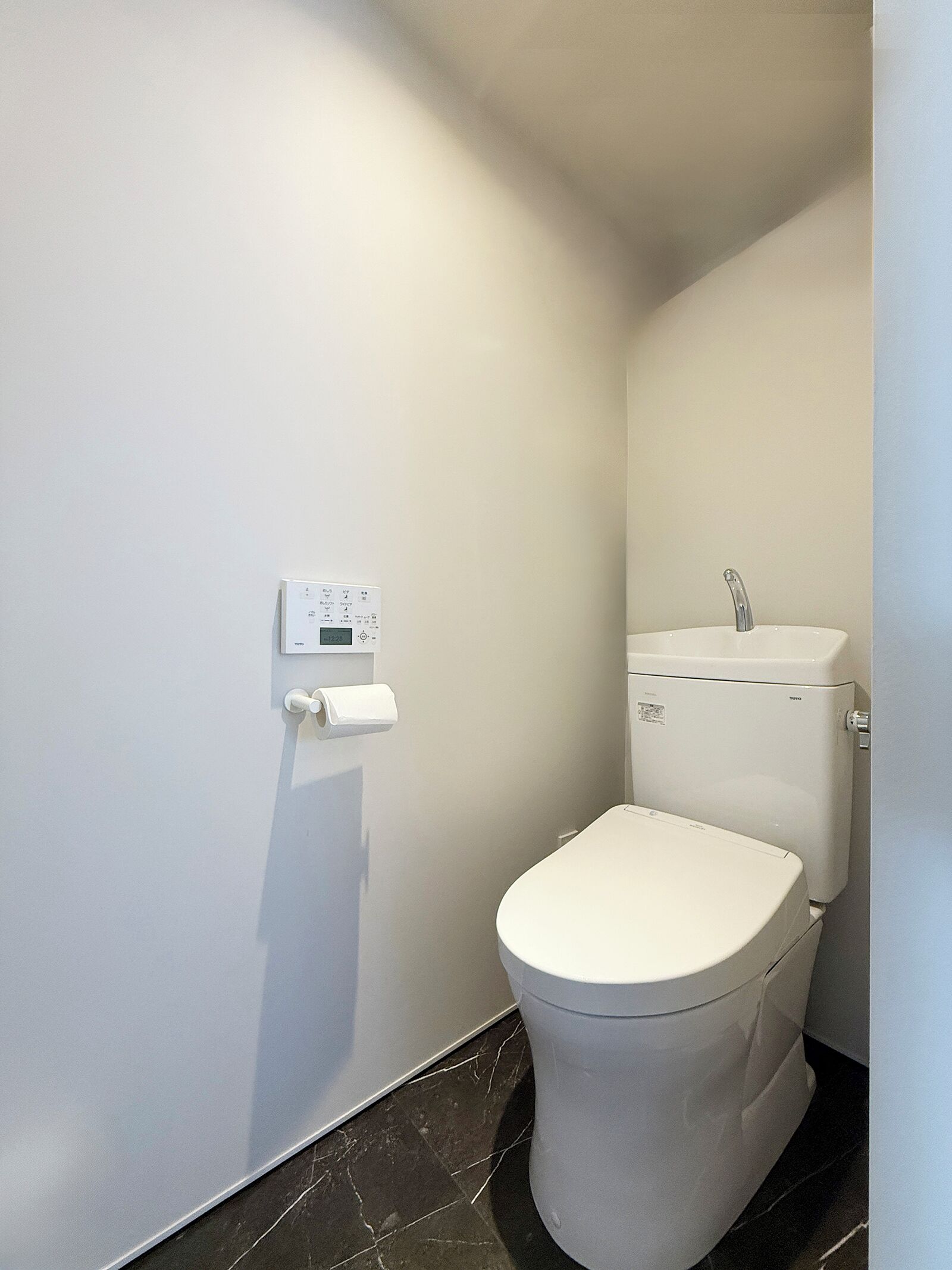 A small, modern bathroom with a toilet, a wall-mounted flush control panel, and a toilet paper holder.