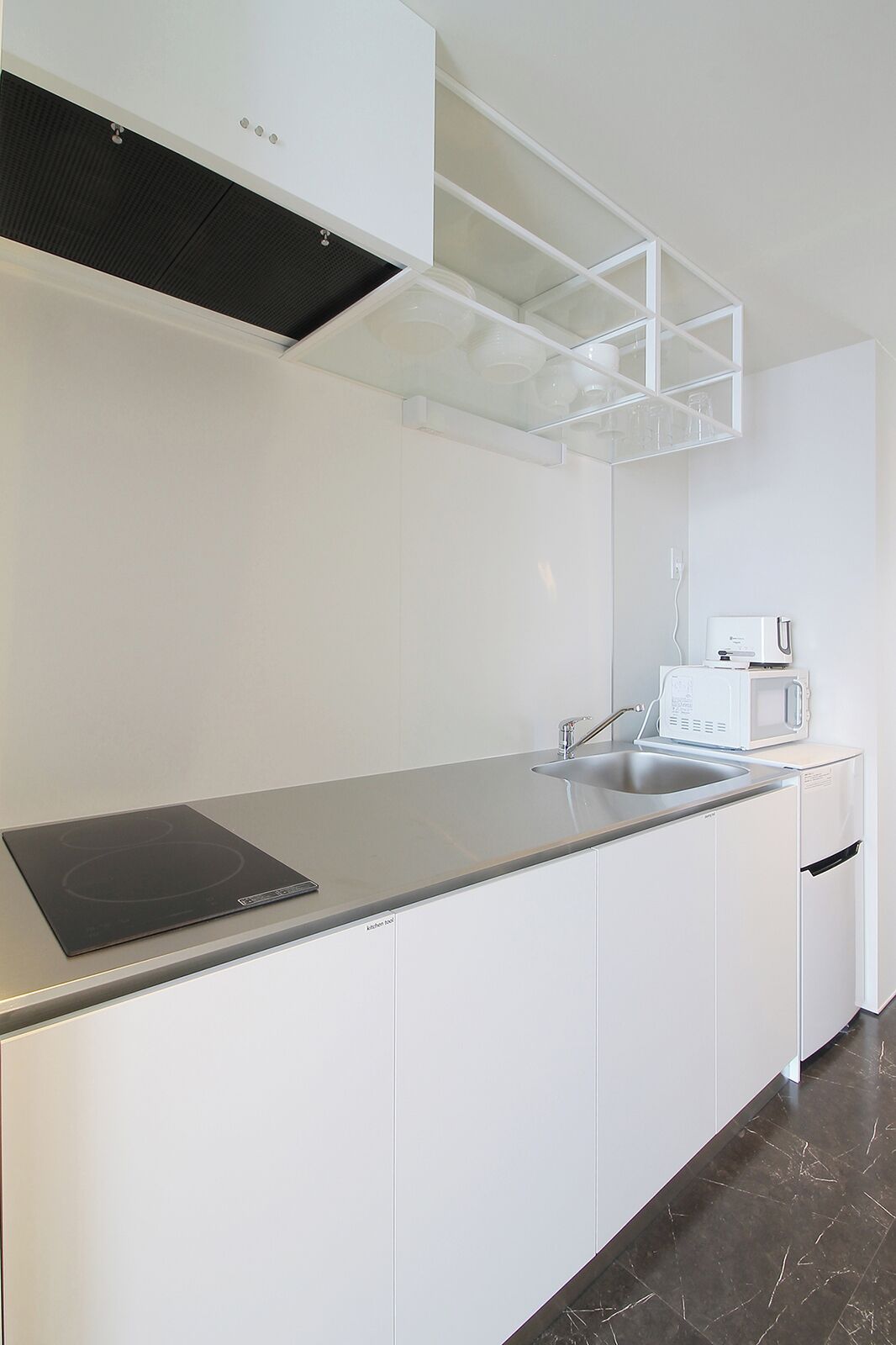 A modern kitchen with white cabinetry, a stainless steel countertop, a built-in microwave, and a black induction cooktop.