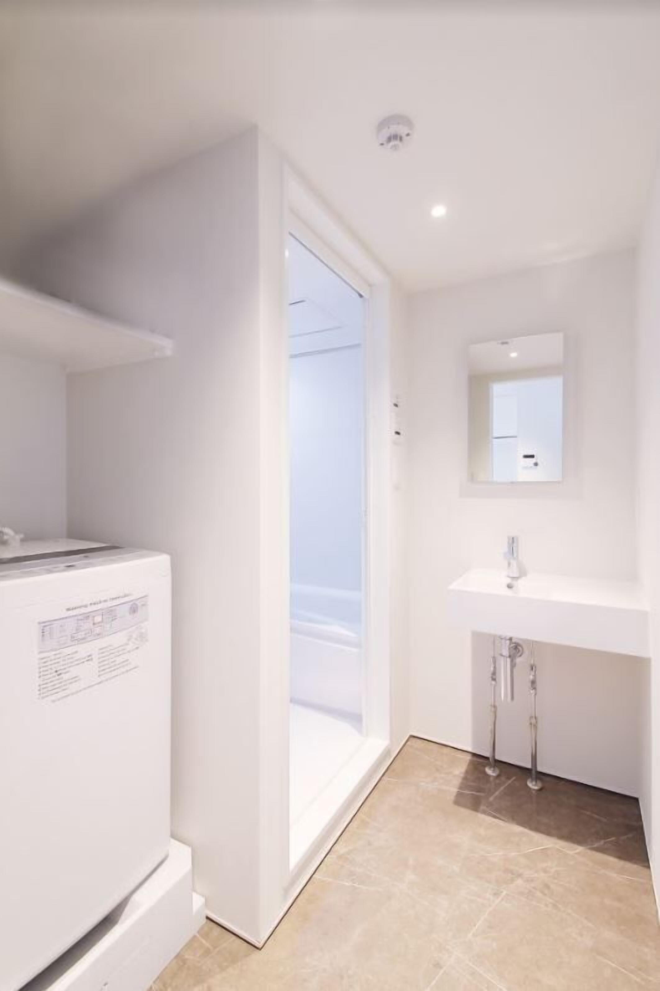 A modern bathroom with a white sink, mirror, and a white appliance, possibly a refrigerator or washer.