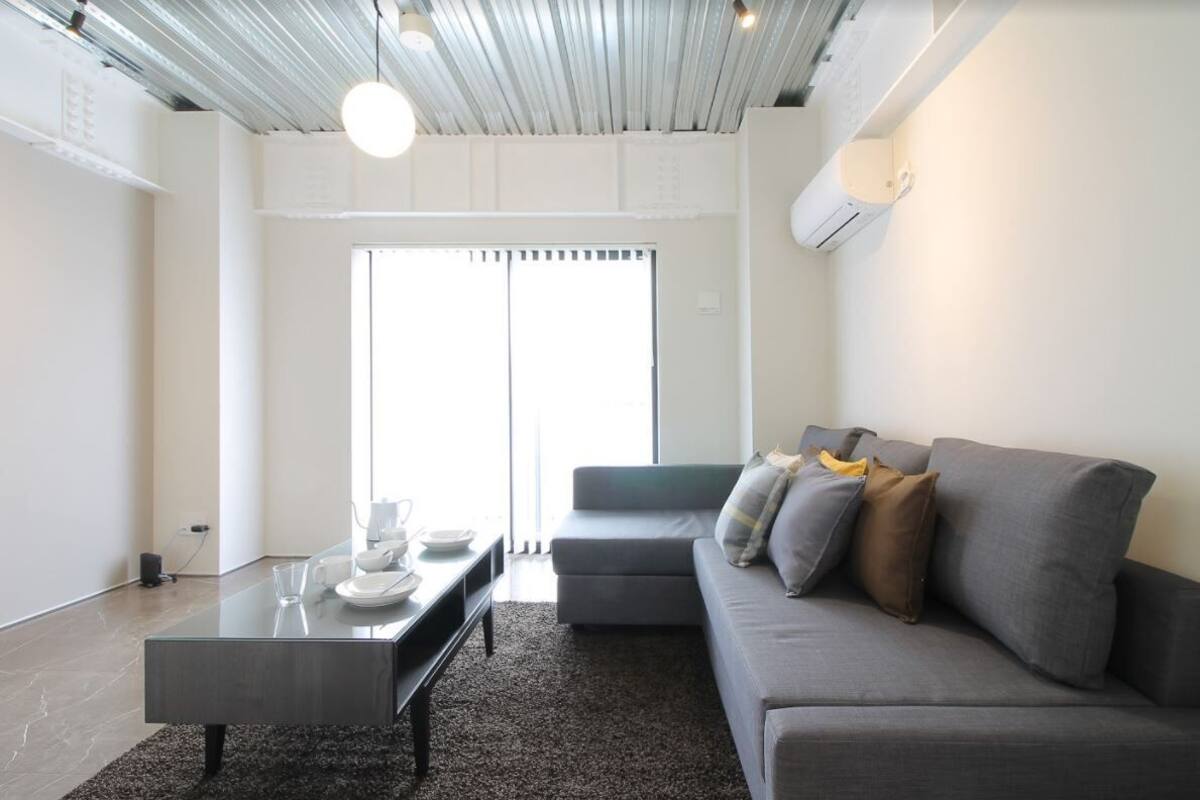 A modern living room with a grey sofa, a glass coffee table, and a dining area with a white table set.