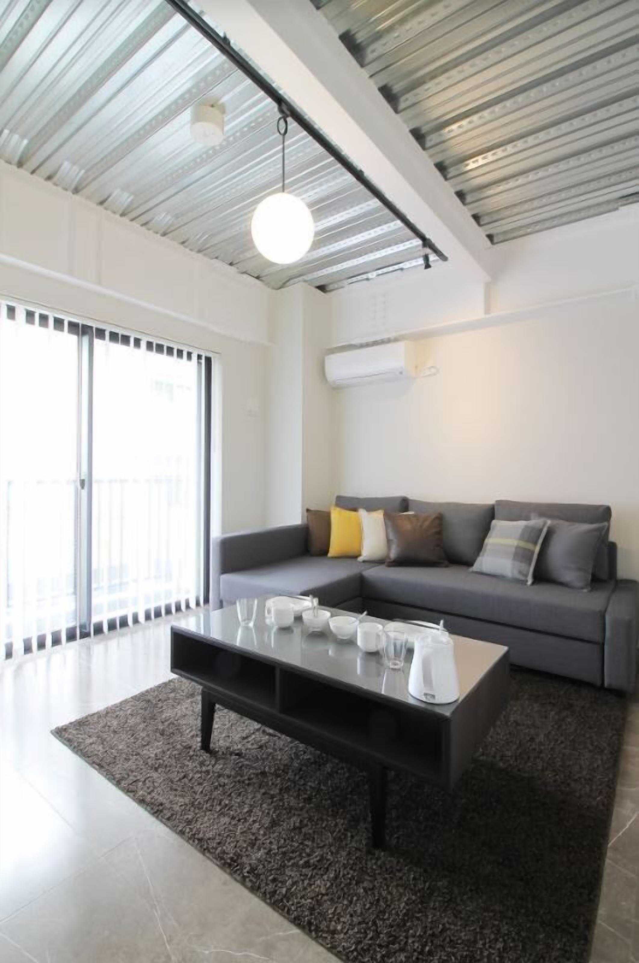 A modern living room with a grey sofa, a coffee table, and a large window with blinds.