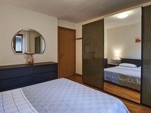 A bedroom with a bed, a dresser, a mirror, a wardrobe, and a bedside table with a lamp. - Ca' Pia by Interhome (San Siro)