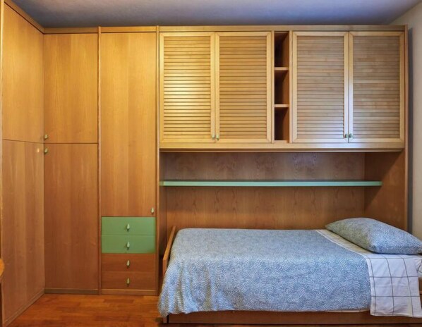 Un dormitorio con armarios de madera, una cama con manta estampada y una cómoda verde.