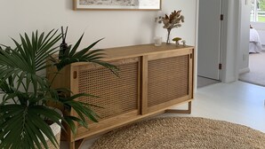 Uma sala de estar moderna com um console de madeira, um quadro grande emoldurado e um tapete redondo de fibras.