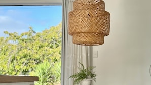 Uma sala de jantar com mesa de madeira e cadeiras pretas, luminária pendente trançada e um vaso de planta sobre a mesa.