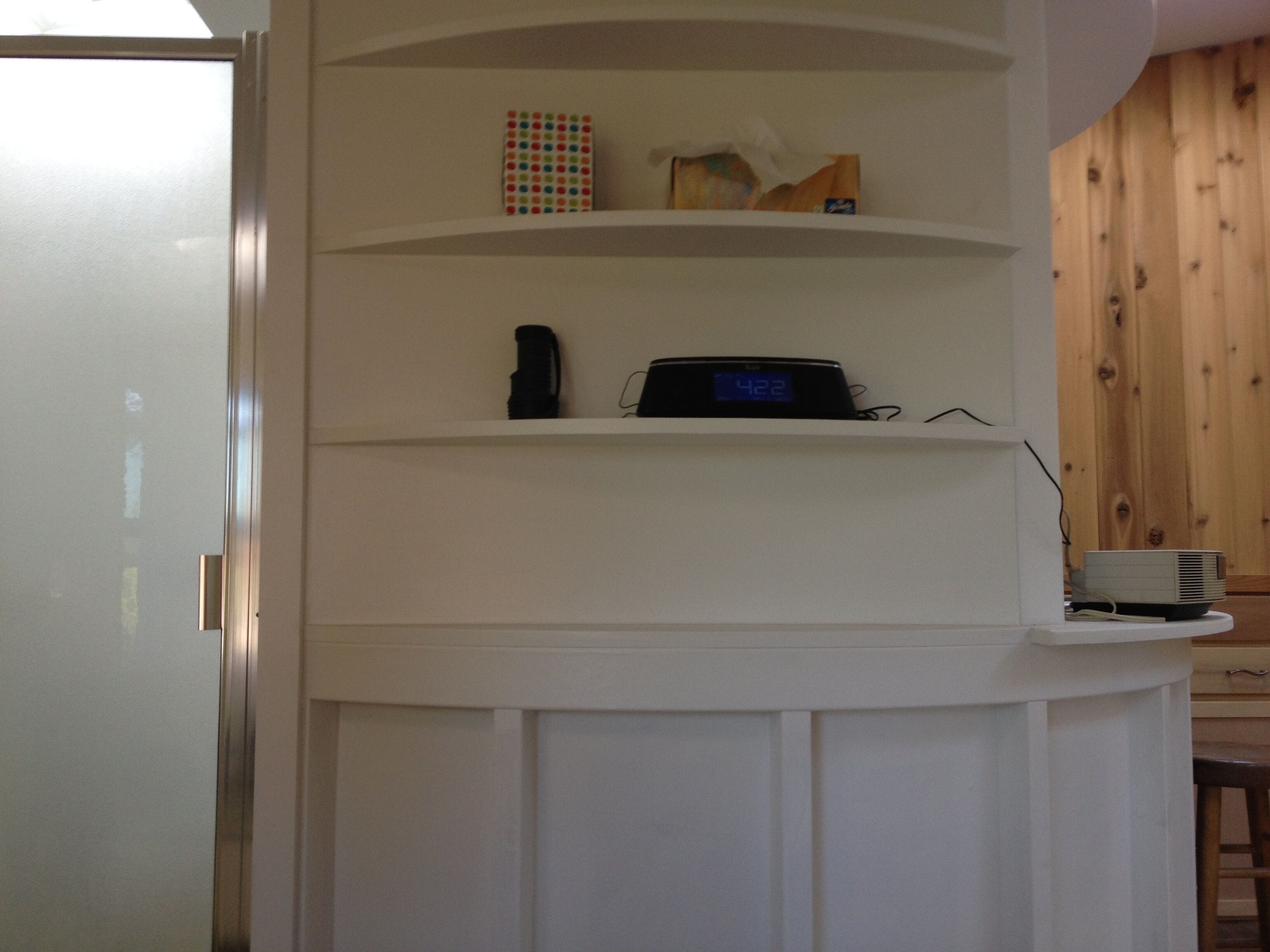 A white built-in shelf unit with a clock displaying 4:22, a black object, and a colorful box.