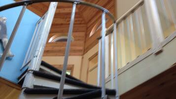 A spiral staircase with metal railings, wooden paneling on the walls, and a circular skylight.