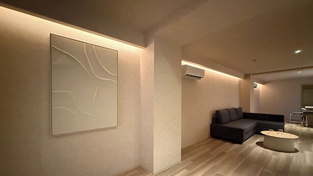A modern living room with a dark sofa, a round coffee table, and a large abstract painting on the wall. - Marumasa 201 (Hiroshima)