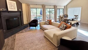 A spacious living room with a fireplace, a ceiling fan, and a large window providing a view of the outdoors. - Hoof Haus in Aspen Valley Country Club in Flagstaff (Flagstaff)
