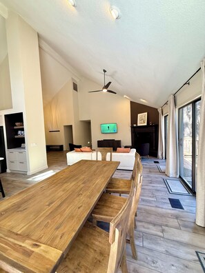 Un salon spacieux avec une table à manger en bois, un canapé et un téléviseur fixé au mur.