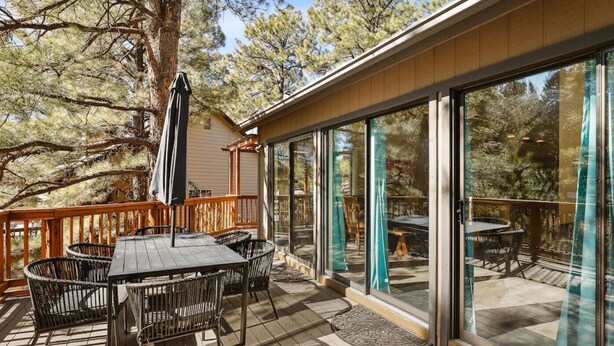 A deck with a table and chairs, a large umbrella, and a glass door leading to a patio area. - Hoof Haus in Aspen Valley Country Club in Flagstaff (Flagstaff)
