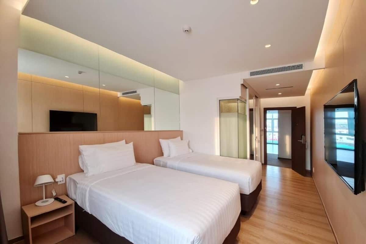 Una habitación de hotel con dos camas, televisión, espejo y suelo de madera.