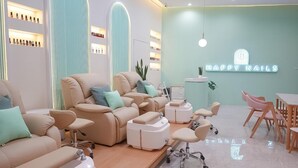 A nail salon with reclining chairs, a reception desk, and shelves of nail products. - Mintel Huamark (Bangkok)