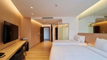 A modern hotel room with a wooden desk, a flat-screen TV, two beds, and a large mirror.