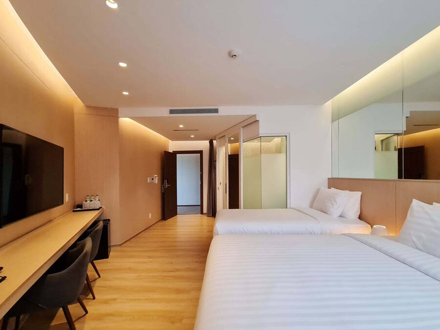 A modern hotel room with a wooden desk, a flat-screen TV, two beds, and a large mirror.