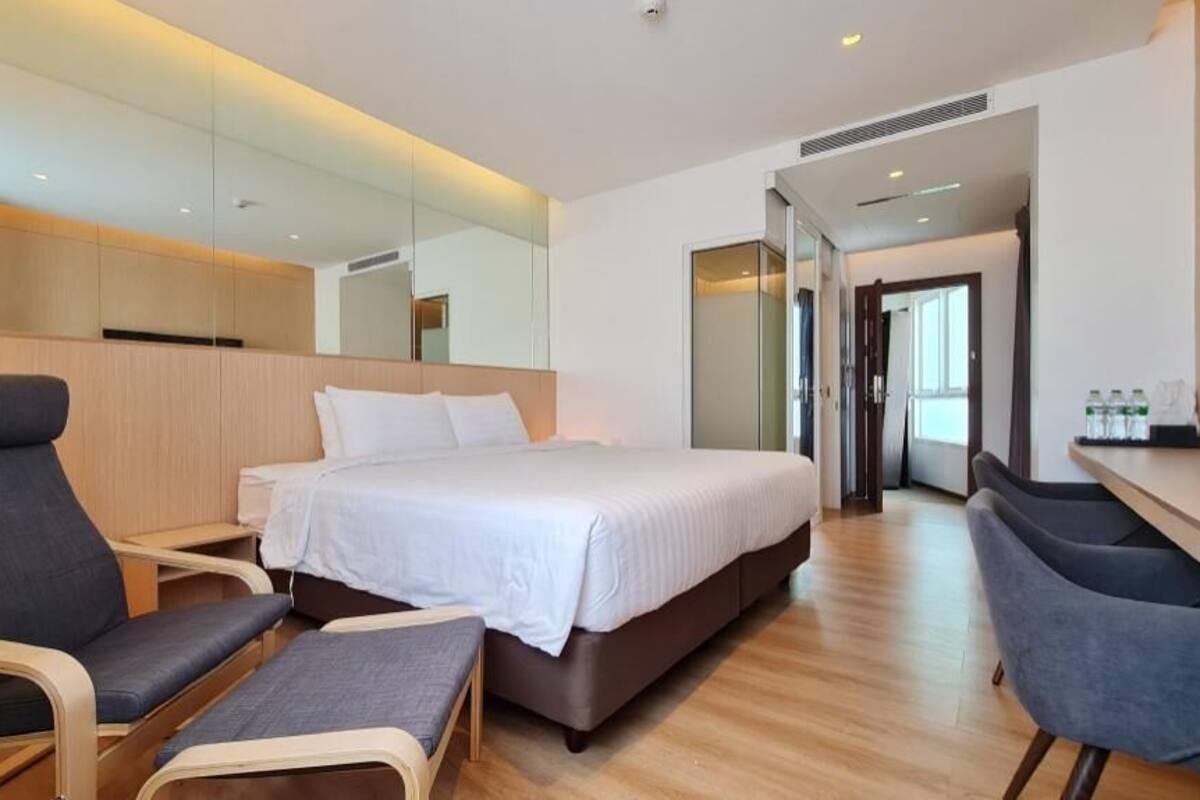 Una habitación de hotel moderna con una cama grande, dos sillones, una mesita y un espejo.