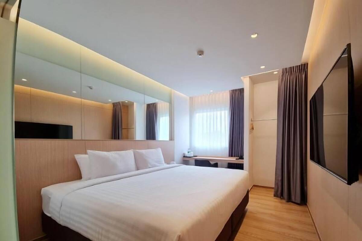 Una habitación de hotel moderna con una cama grande, un escritorio, un televisor de pantalla plana y un espejo amplio.