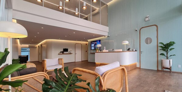 A spacious lobby with a reception desk, wicker chairs, and a large plant. - Mintel Huamark (Bangkok)