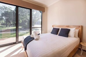 A bedroom with a large window, a bed with pillows, and a view of a park.