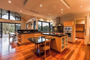 A modern kitchen with a large island, wooden cabinets, and a view of the outdoors.