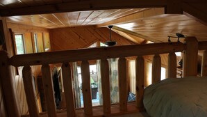 A bedroom with a wooden ceiling, a bed, and a view of the outside through a window.