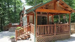 A wooden cabin with a covered porch and a staircase leading to a deck.
