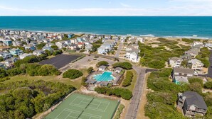 Ett flygbildsfoto av ett bostadsområde vid kusten med hus, en tennisbana och en swimmingpool.